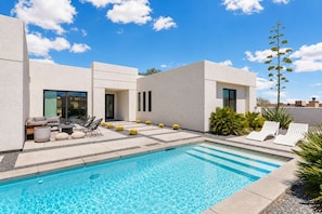Un espace piscine moderne avec une piscine à l’eau d’un bleu limpide, des chaises longues et une terrasse agrémentée de sièges et de plantes.