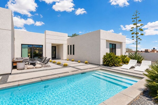 Ein moderner Poolbereich mit einem klaren, blauen Pool, Liegestühlen und einer Terrasse mit Sitzgelegenheiten und Pflanzen.