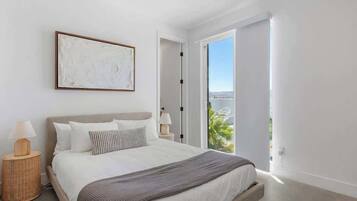 Un dormitorio moderno con una cama grande, vistas a zonas verdes a través de una puerta abierta y un cuadro abstracto enmarcado en la pared.