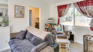 A cozy living room with a sofa, a chair, a bookshelf, and a window with curtains. - Private Horse Stall: Unplug at Shingletown Home! (Shingletown)