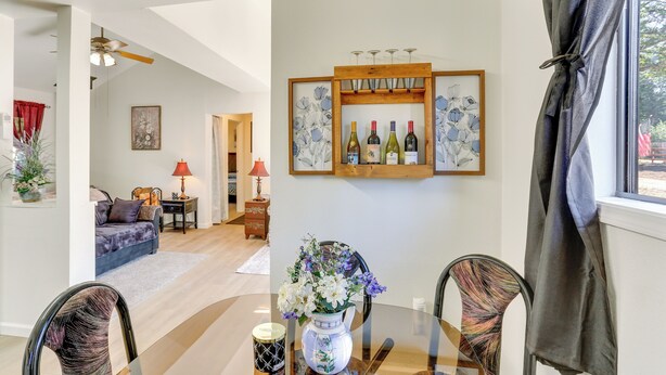 A dining area with a glass table, chairs, a vase with flowers, and a wine rack with bottles. - Private Horse Stall: Unplug at Shingletown Home! (Shingletown)