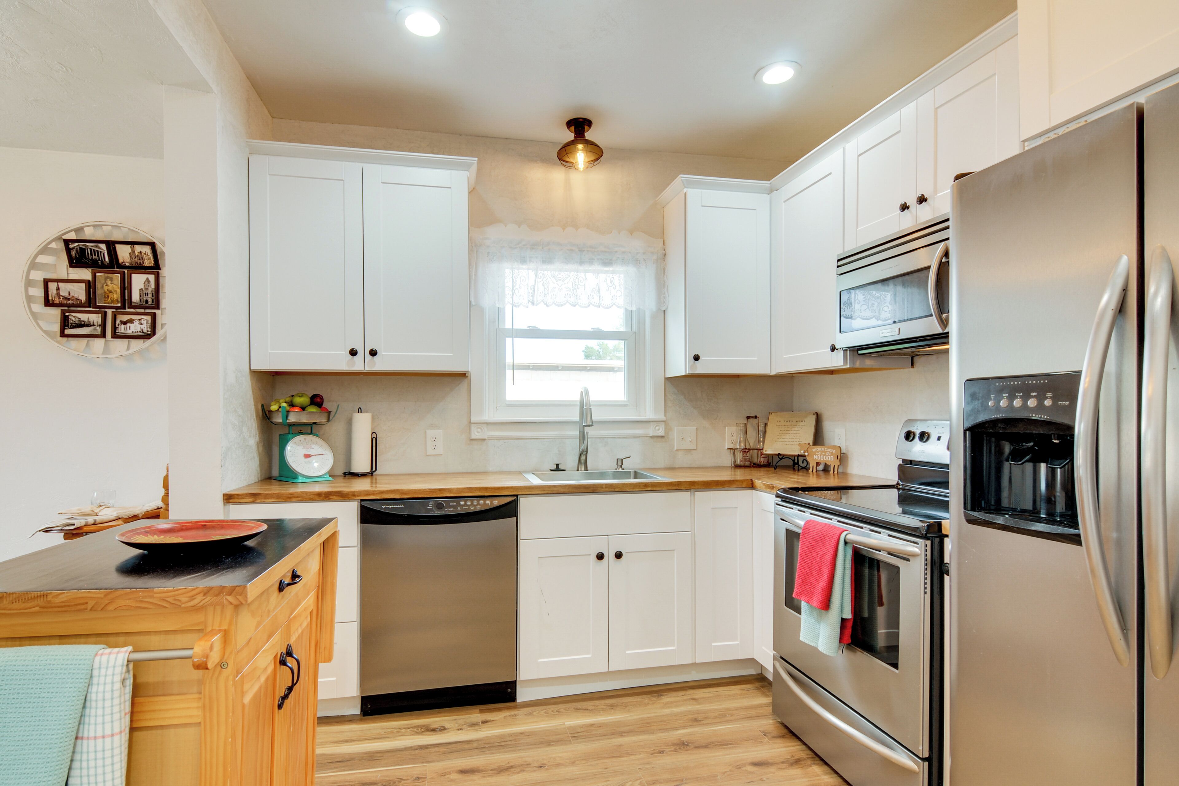 A modern kitchen with white cabinets, stainless steel appliances, a wooden countertop, and a window with a white valance.