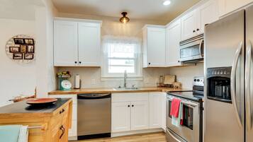 A modern kitchen with white cabinets, stainless steel appliances, a wooden countertop, and a window with a white valance.