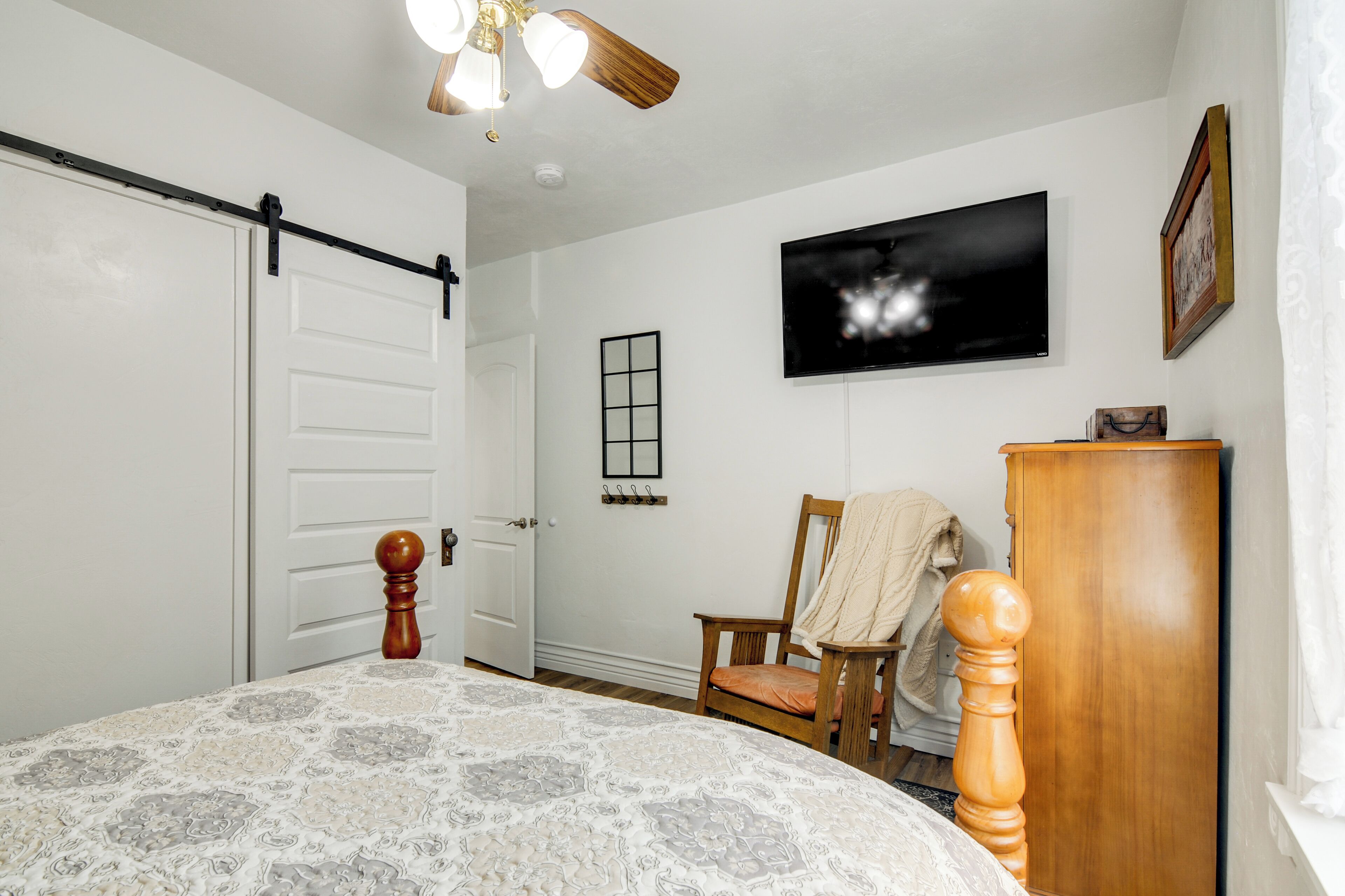 A bedroom with a bed, a wooden dresser, a chair, a television, and a sliding door.