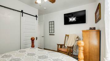 A bedroom with a bed, a wooden dresser, a chair, a television, and a sliding door.