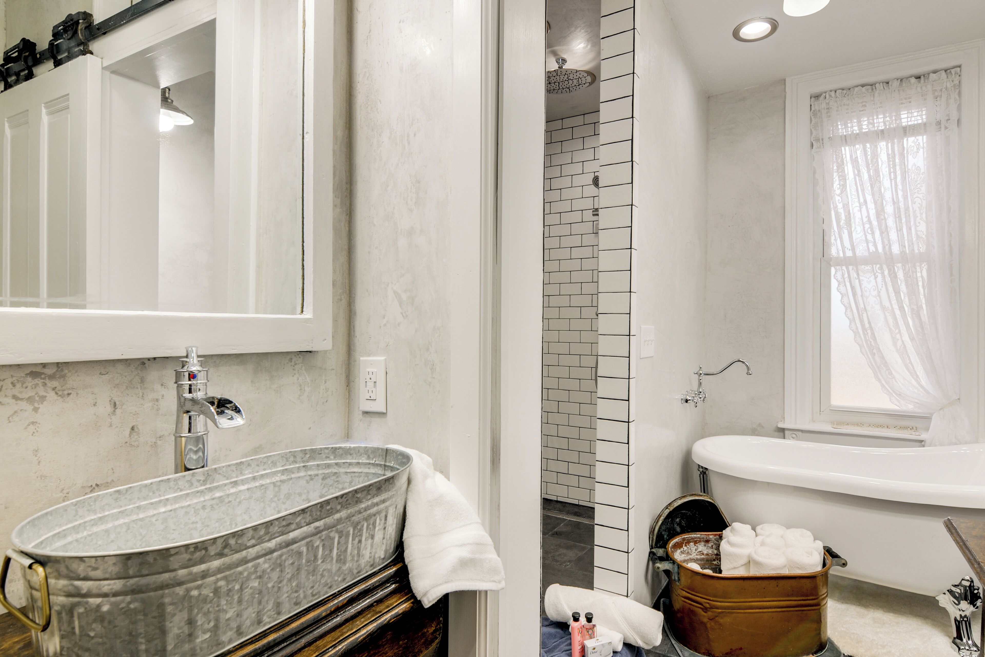 A bathroom with a large metal basin sink, a bathtub, and a shower area.
