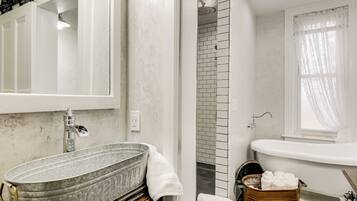 A bathroom with a large metal basin sink, a bathtub, and a shower area.