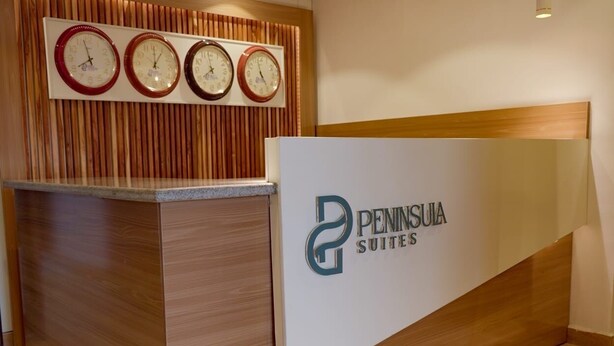 A reception desk with a logo for Peninsula Suites, a wooden wall with clocks, and a wooden floor. - Peninsula Suites (Bwari)