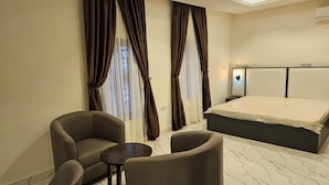 A hotel room with a bed, two armchairs, a small table, and curtains. - Peninsula Suites (Bwari)