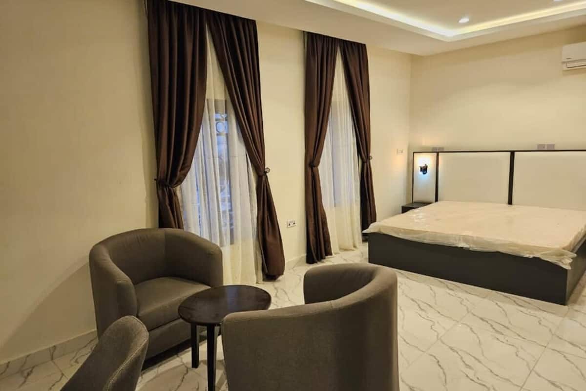 A hotel room with a bed, two armchairs, a small table, and curtains.