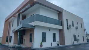 A modern two-story building with a flat roof, large windows, and a balcony on the second floor. - Peninsula Suites (Bwari)