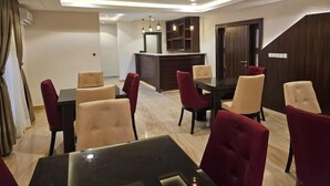 A modern dining area with a central island, red and beige upholstered chairs, and recessed ceiling lighting. - Peninsula Suites (Bwari)