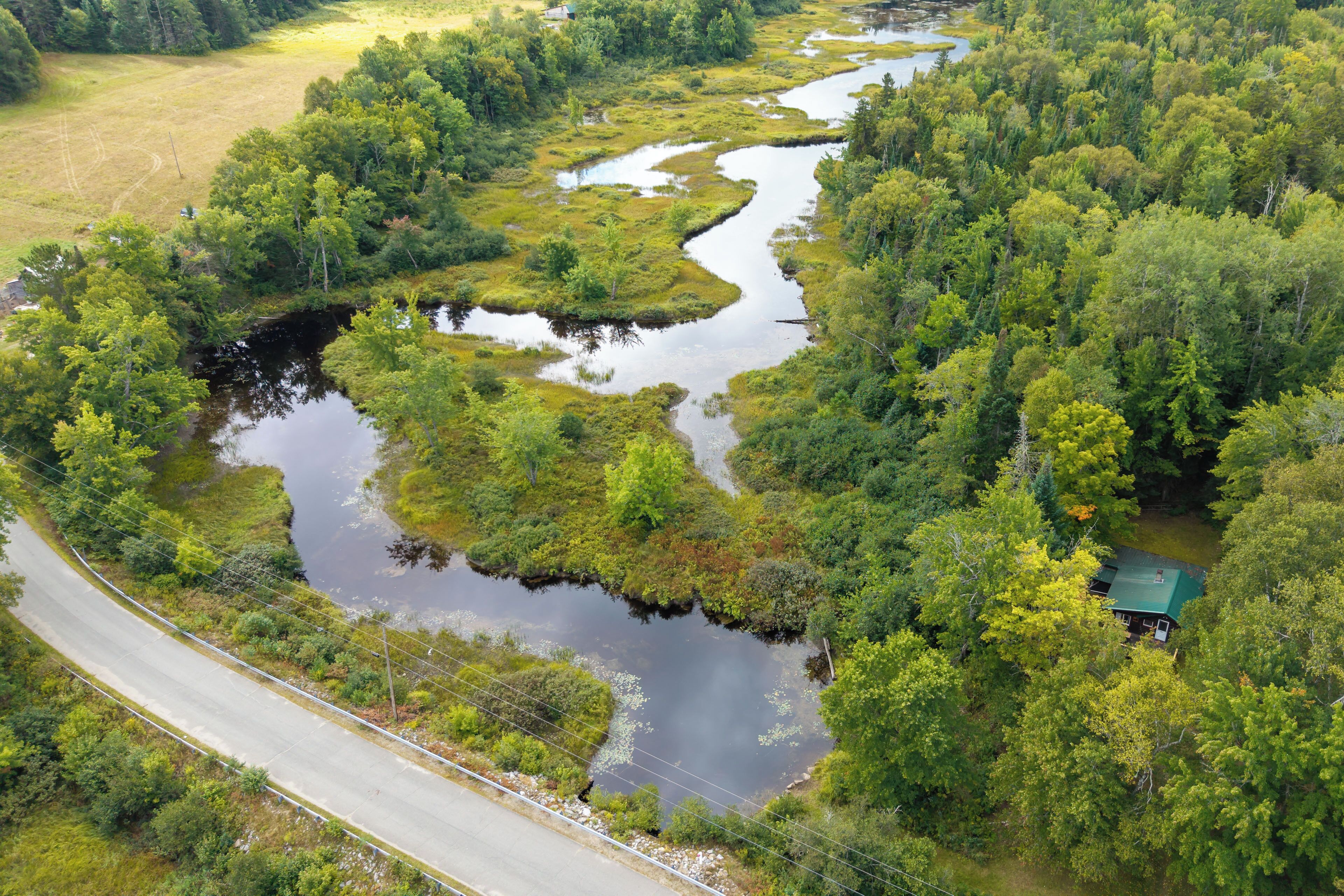 An aerial view of a river winding through a forested area with a house on the right bank.