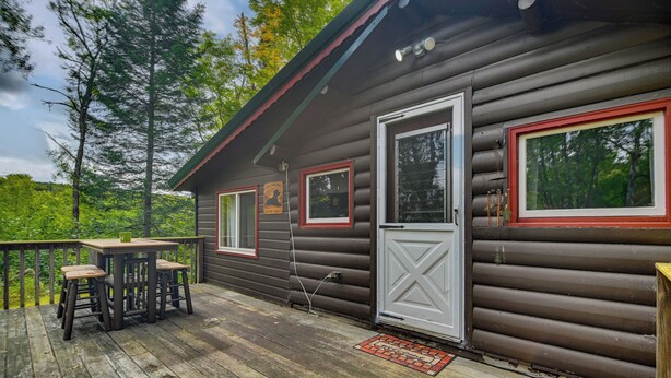 A log cabin with a deck, a table, and two chairs. - Deck + Fire Pit: Nature Lover's Retreat in Maine! (Errol)