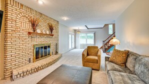 A living room with a brick fireplace, a sofa, a chair, and a staircase leading to an upper floor. - Rural & Private Dover Retreat: Close to Wineries! (Dover)