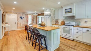 A kitchen with wooden flooring, white cabinets, a central island with bar stools, and a stove.