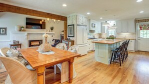 A spacious kitchen with a wooden dining table, white cabinets, and a large island with bar stools.