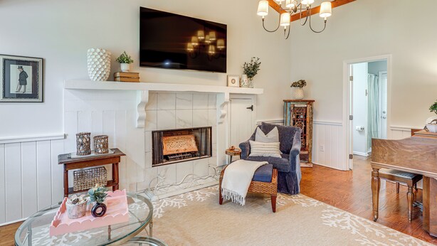A living room with a fireplace, a television mounted above it, a chandelier, a piano, and a comfortable seating area.