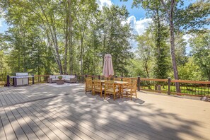 A wooden deck with outdoor furniture, a grill, and a view of a forested area.