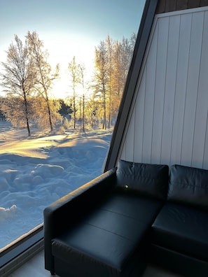 A room with a view of a snowy landscape, a black leather sofa, and a window with blinds.