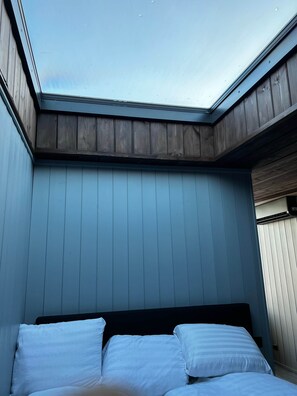 A room with a skylight, a bed with white bedding, and wooden paneling on the walls.