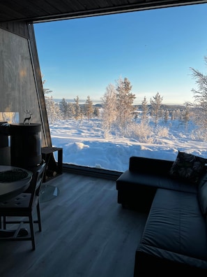 A modern interior with a large window, a sofa, a dining table, and a decorative deer figurine. - Lodge Arctic 3– sauna, toit vitré & vue lac Inari (Inari)