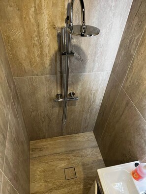 A shower with a handheld showerhead and a fixed overhead showerhead, a small rectangular vent on the floor, and a white sink with a bottle of soap. - Lodge Arctic 3– sauna, toit vitré & vue lac Inari (Inari)