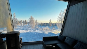 A modern interior with a large window, a sofa, a coffee table, and a fireplace. - Lodge Arctic 4 – sauna, toit vitré & vue lac Inari (Inari)