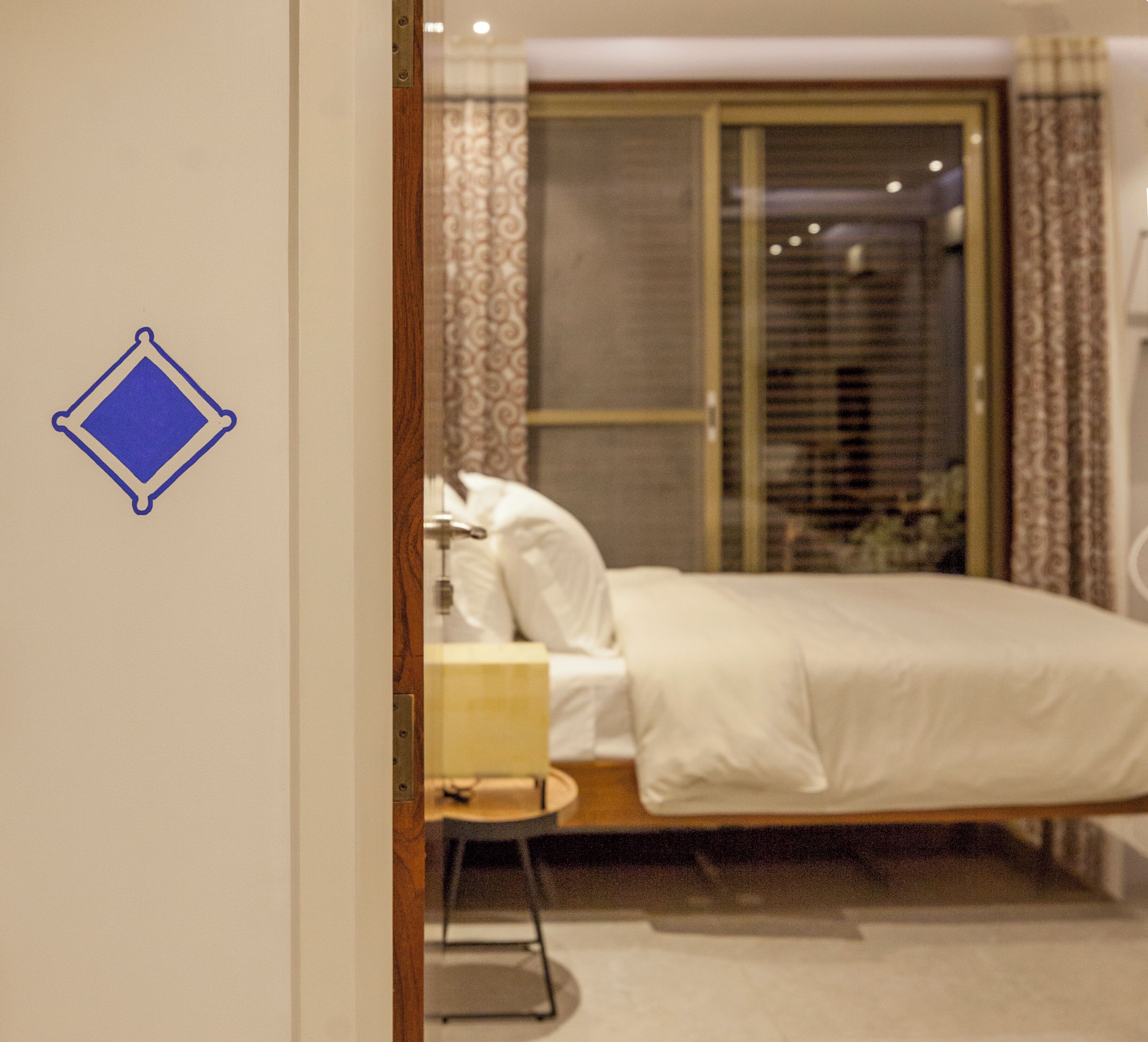 Una habitación de hotel con una cama, una mesita de noche, una lámpara y una ventana con cortinas.