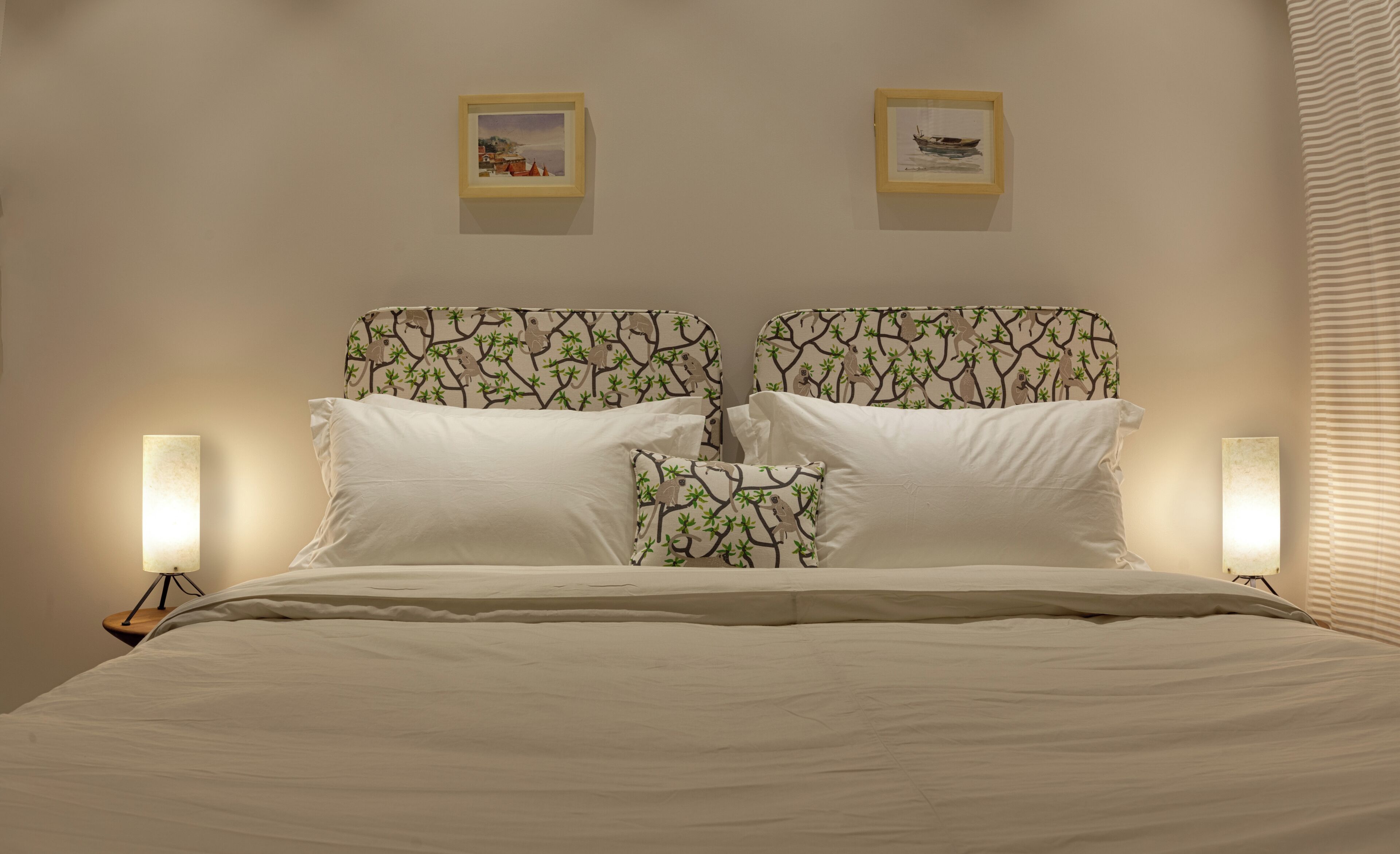 A bed with a headboard featuring a tree pattern, two bedside lamps, and two framed pictures on the wall.