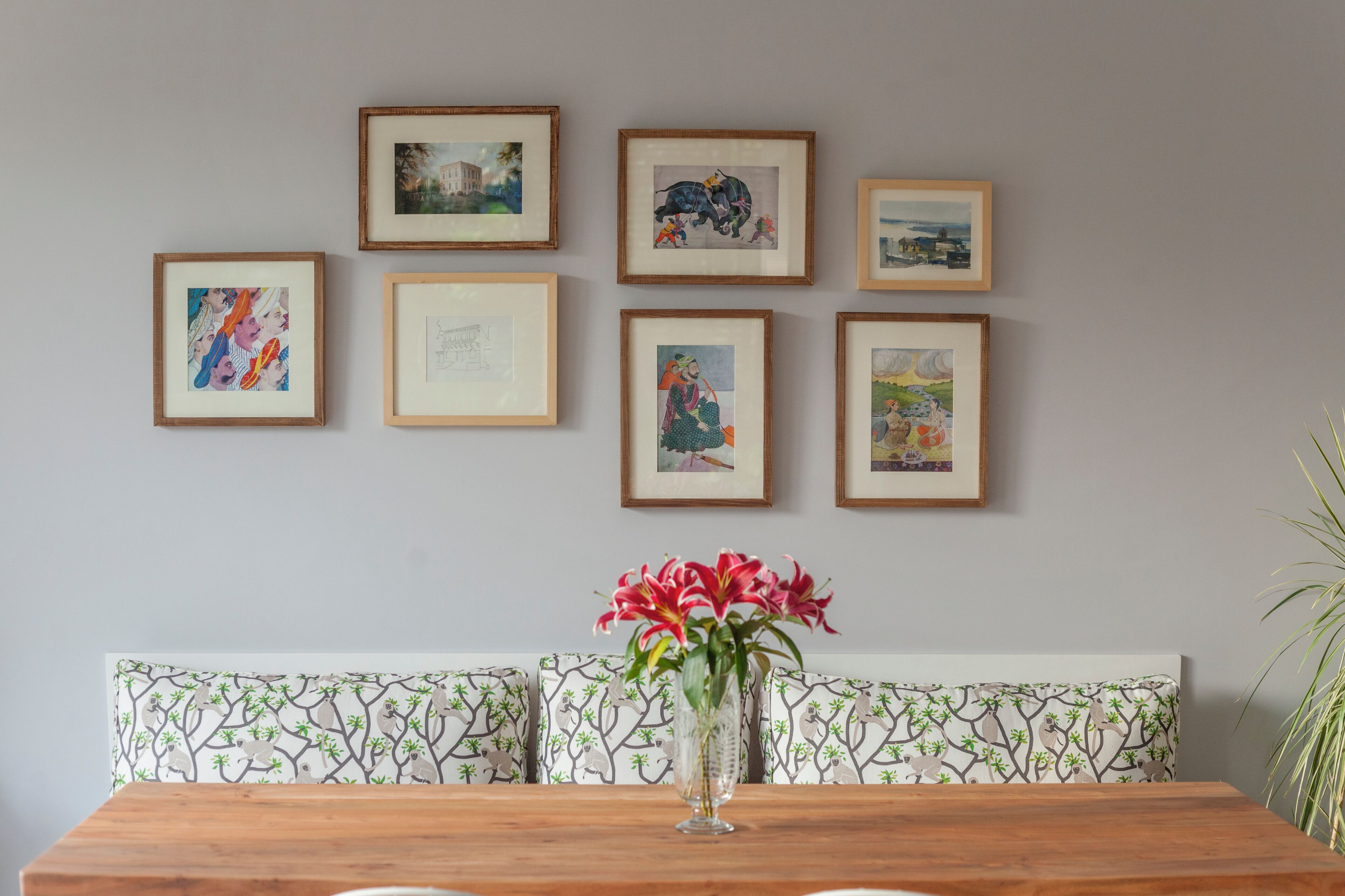Uma sala de jantar com mesa de madeira, um vaso de flores e um banco com almofadas estampadas.