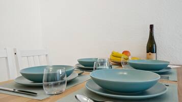 A dining table set with blue plates, glasses, and cutlery, accompanied by a bottle of wine and a bowl of fruit.