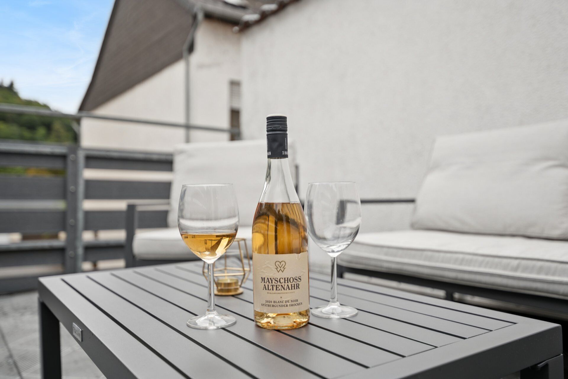 A bottle of wine and two glasses on a table outdoors.