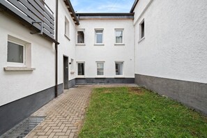 A narrow courtyard with a paved walkway, a grassy area, and a building with multiple windows and a door. - Haven of peace for people & dogs with terrace (Andernach)