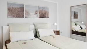A bedroom with two beds, a nightstand, a bedside lamp, and three beach-themed wall art pieces. - Haven of peace for people & dogs with terrace (Andernach)