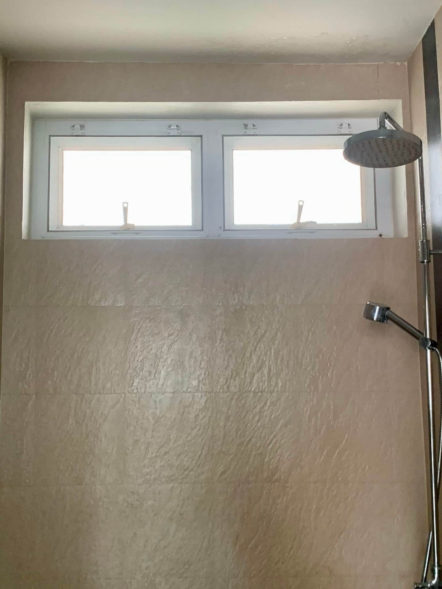 Ein Badezimmer mit zwei Fenstern, einer Duschbrause und einem Handtuchhalter.