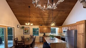 Une cuisine spacieuse avec des meubles en bois, un grand îlot central et un plafond orné d’un lustre original en forme de bois de cerf.