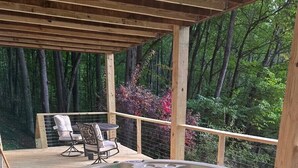 Un bain à remous installé sous une terrasse en bois, avec vue sur une forêt.