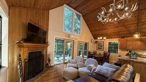 Un intérieur de chalet chaleureux avec une cheminée, des sièges confortables, un coin repas et de grandes fenêtres.