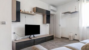 A modern living room with a flat-screen TV, built-in shelves, and a grey sofa. - Villa 'Il Gelsomino' with Mountain View, Private Terrace, EV Charging & Wi-Fi (Cuasso al Piano)