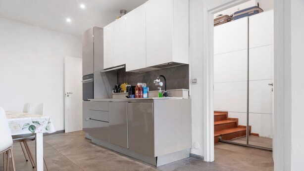A compact kitchen with a dining table, a built-in oven, and a small countertop with various items. - Villa 'Il Gelsomino' with Mountain View, Private Terrace, EV Charging & Wi-Fi (Cuasso al Piano)