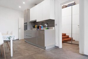 Een compacte keuken met een eettafel, een inbouwoven en een klein aanrecht met diverse spullen.