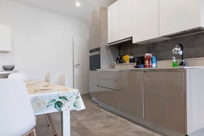 A modern kitchen with stainless steel appliances, a dining table with a floral tablecloth, and a small countertop with various items.