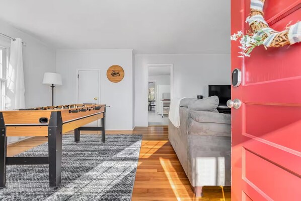 Una sala de estar moderna con una mesa de futbolín, un sofá gris y una puerta roja.