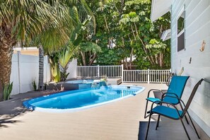 A swimming pool with a white fence, a blue chair, and tropical plants.