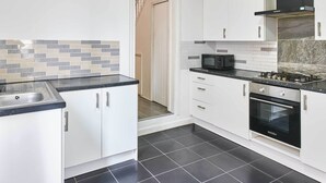 Cozinha com armários brancos, bancada preta, micro-ondas e forno.