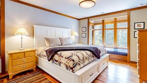 Une chambre avec un grand lit, un plancher en bois et une fenêtre équipée de stores.