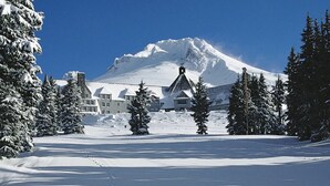 Un paysage enneigé, avec une montagne en arrière-plan et un bâtiment doté de nombreuses fenêtres et d’une cheminée.