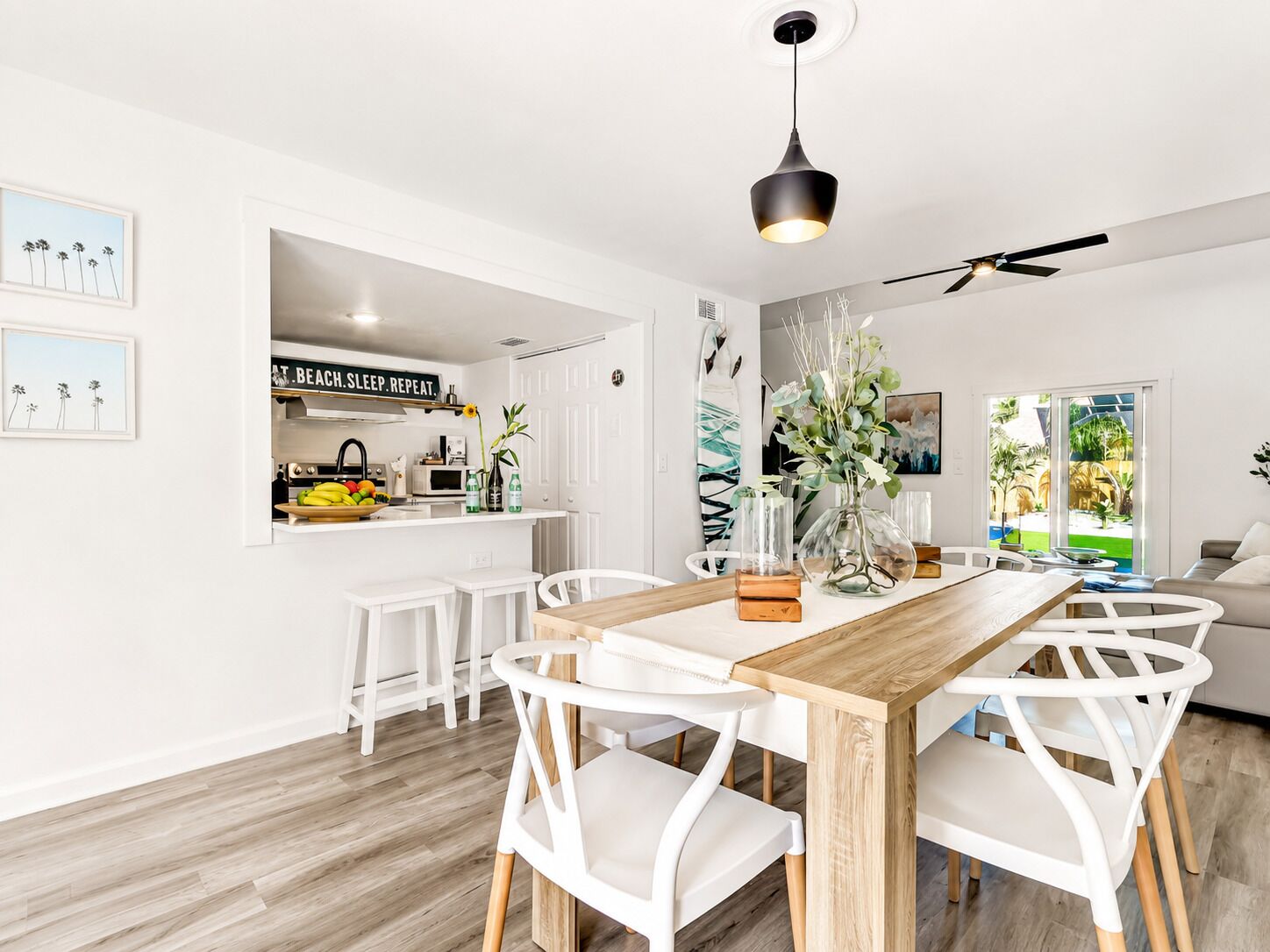 Une cuisine moderne avec des meubles blancs, une table à manger en bois et un ventilateur de plafond.