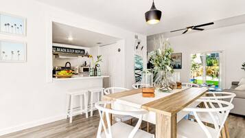 Une cuisine moderne avec des meubles blancs, une table à manger en bois et un ventilateur de plafond.